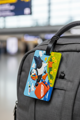 Colorful Iceland puffin luggage tag with a cartoon puffin carrying an orange suitcase, attached to a black strap, playful travel accessory