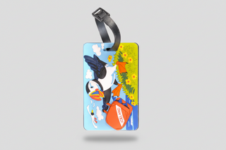 Colorful Iceland puffin luggage tag with a cartoon puffin carrying an orange suitcase, attached to a black strap, playful travel accessory