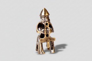 Metallic figurine of a character holding an ankh on a white background