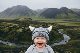 Gray knit baby hat with white horns and a brand tag on a white background