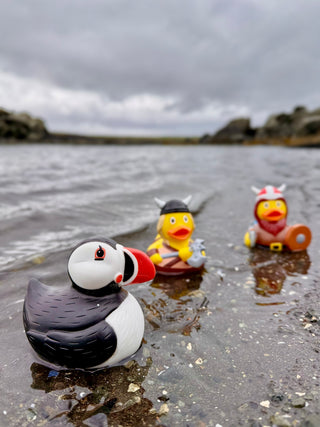 Three rubber duck toys on a beach with a cloudy sky