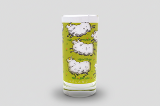 Iceland sheep glass milk cup with playful cartoon sheep design on green background, Iceland souvenir drinking glass.