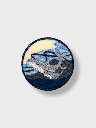 Round iron-on embroidered patch featuring a whale swimming in the ocean, inspired by Icelandic marine life.