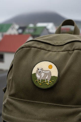 Circular patch with embroidered design of a cow in a field on a beige background on a backpack