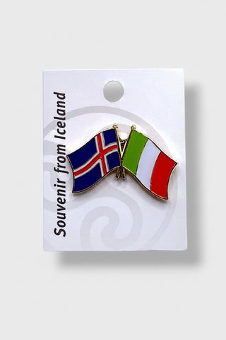 A small enamel lapel pin shaped like two crossed flags, one Icelandic flag and one Italian flag, attached to a white display card. The card reads 'Souvenir from Iceland' 
