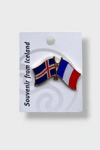 An enamel lapel pin depicting the flags of Iceland and France in a crossed flag design, mounted on a white card backing printed with 'Souvenir from Iceland'  