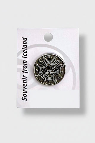 A round silver-toned metal souvenir pin reading 'Iceland' with a Celtic knot design, mounted on a white backing card that says 'Souvenir from Iceland' 