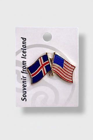 A small enamel lapel pin shaped like two crossed flags, one Icelandic flag and one American flag, attached to a white display card. The card reads 'Souvenir from Iceland' 