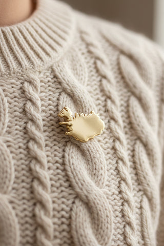 A small gold-toned souvenir pin shaped like the map of Iceland