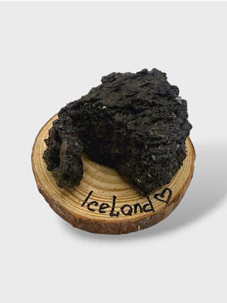 Black rock on a wooden coaster with 'Iceland' written on it against a white background