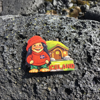 Fridge magnet with a cartoon character in a red outfit and hat, standing in front of a house with 'Iceland' text on a white background.
