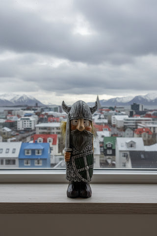 A small Viking figurine with a silver horned helmet, brown beard, green shield, and orange cheeks
