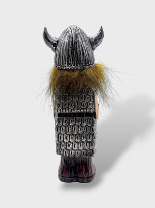A small Viking warrior figurine shown from the back, wearing a horned helmet, scale armor, and a brown fur collar, photographed on a light gray background.