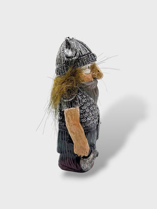 A small Viking figurine with a textured silver helmet, chainmail armor, brown beard, and a light tan arm, shown against a light gray background with a soft shadow.