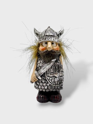 A small decorative figurine of a Viking warrior with a horned helmet, silver-toned armor, a brown beard, and wispy blond hair, shown against a light gray background.