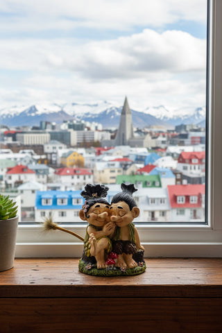 A whimsical gnome figurine depicting two kissing fairies with black hair, wearing earthy green and brown outfits, sitting on a grassy base with red mushrooms and the word 'Iceland' printed on it.