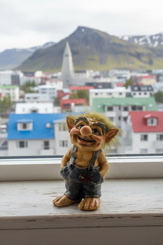 A small gnome figurine with wild brown hair, large pointed ears, and a wide toothy grin, wearing dark blue-gray denim overalls over tan skin