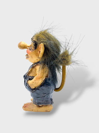 A small sculpted figurine of a goblin-like character with large ears, a long nose, wild brown hair, and a dark blue apron, photographed on a light gray background.