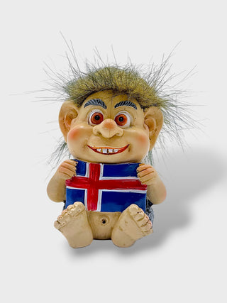 A small troll figurine with wild hair holding an Iceland flag, shown against a light gray background.