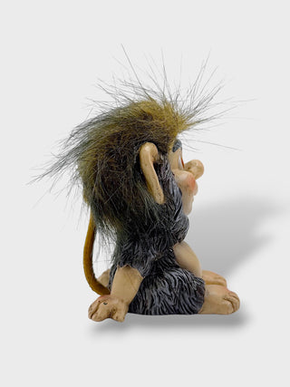 A small seated fantasy creature figurine with large beige ears, a long thin spiky mane in brown and black, and gray fur, shown against a light gray background.