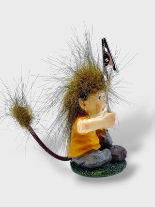 A whimsical figurine of a child dressed as a hedgehog, sitting on a small green base. The figure wears an orange shirt and gray pants, holding a fishing rod with a hook and line.