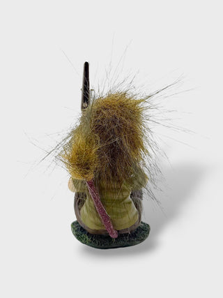 A small handmade fishing lure or bait featuring a green body, a dark black hook, and a large, messy golden-brown hair-like tail with a pinkish-purple accent, shown from the back on a light gray background.