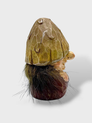 A unique sculptural figurine resembling a stylized mushroom with a textured olive-brown cap, a dark brown and black furry base, and a small beige face detail, photographed on a light gray background.