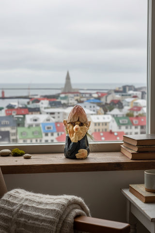 A small sculpted gnome figurine with a brown conical hat, pale beige face and hands, dark blue clothing, and short greenish hair