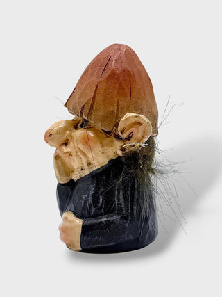 A small carved figurine of a gnome or goblin character with a brown hat, pale skin, dark beard, and black clothing, photographed on a light gray background.