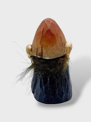 A small sculptural figurine or decorative object with a pointed orange-brown top, pale gold side details, dark brown hair-like texture, and a dark blue faceted base, photographed on a light gray background.