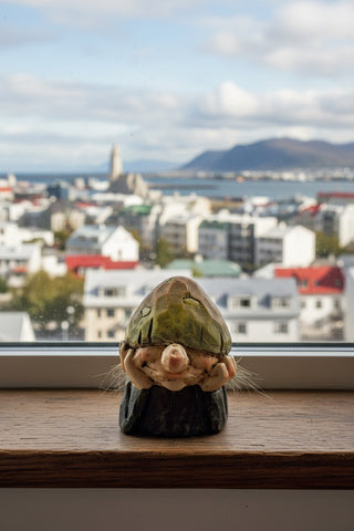 A small decorative figurine shaped like a gnome or character, made from natural materials including a green shell, peach-colored shell pieces,