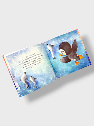 An open children's picture book showing two illustrated ocean pages with dolphins and a puffin underwater, photographed on a light gray background.