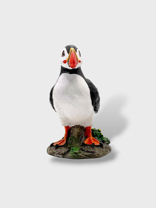 A small puffin figurine standing on a rocky base with green moss details, photographed against a light gray studio background.
