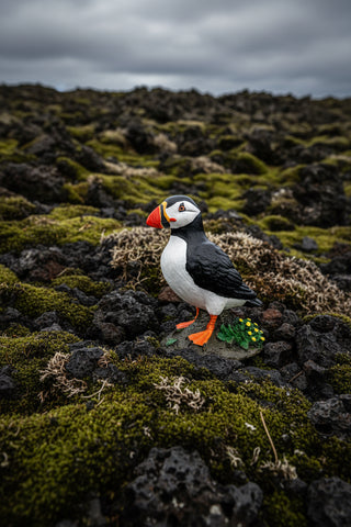 Realistic Iceland puffin figurine standing on a rocky base with small yellow flowers
