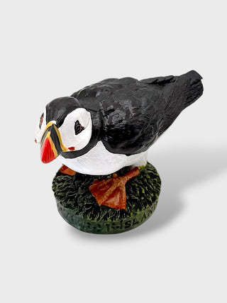 A decorative puffin figurine standing on a textured green base against a light gray background.