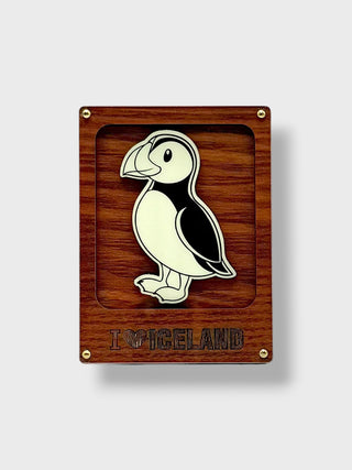 A rectangular wooden plaque featuring a puffin illustration in black and white with the text 'I'M ICELAND' engraved below, set against a light gray background.