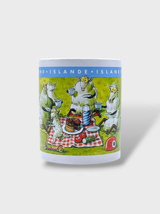 A white ceramic mug featuring a colorful cartoon illustration of sheep having a picnic on a red-and-white checkered blanket, with the text 'ÅLAND-ISLANDEN-ISLANDEN' printed in blue around the top band.