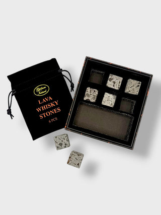 A boxed set of six lava stone whisky stones shown open beside a black drawstring pouch. The stones have a light gray and black mottled volcanic texture, and the pouch is printed with the product name and a small gold logo.
