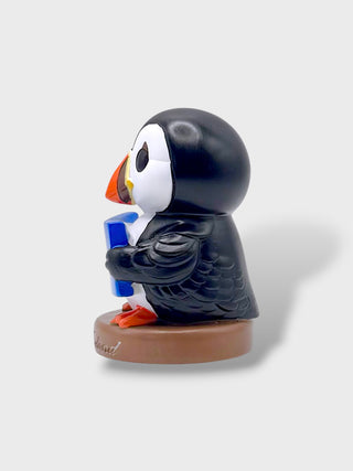 A small puffin figurine holding a blue mug, standing on a round brown base against a light gray background.