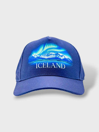 A royal blue baseball cap featuring a graphic of the Icelandic landscape with the Aurora Borealis and the word 'ICELAND' printed in white on the front, set against a light gray background.