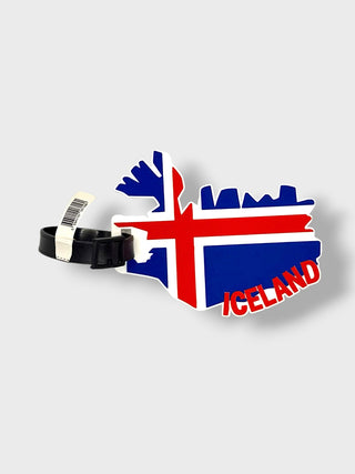 An Iceland map-shaped luggage tag featuring the Icelandic flag and skyline, with 'ICELAND' written in red text, attached to a black strap on a light gray background.