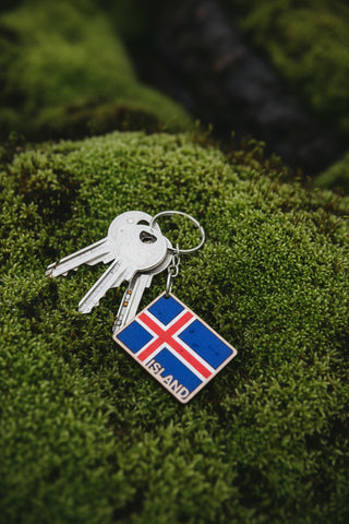 An Iceland flag keychain with a diamond-shaped pendant, attached to a gold-colored split ring and displayed on its brown cardboard backing card. The backing card features the text 'NORDIC KEYCHAIN' and 'Handcrafted with love'.