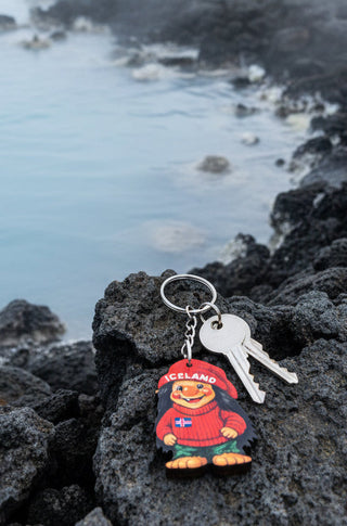 An Iceland-themed souvenir keychain on a brown cardboard backing card. The keychain features a cartoon penguin wearing a red beanie and red sweater with the word 'ICELAND' and a small Icelandic flag.