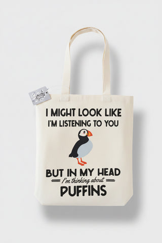 A white canvas tote bag with a humorous text print and a puffin illustration, shown against a light gray background.