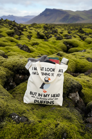 A white canvas tote bag with a humorous text print and a puffin illustration, shown against a light gray background.