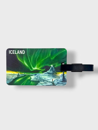 A rectangular luggage tag featuring an illustration of Iceland's northern lights over icy mountains, with a black strap attached on a light gray background.